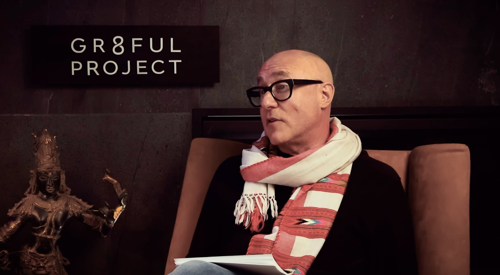 Gr8ful Podcast host mid-episode, seated in front of the Gr8ful Project sign